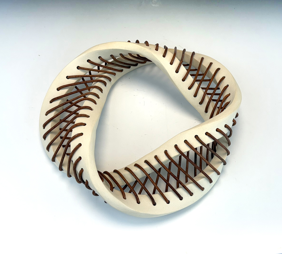 Ceramic sculpture of a Mobius band with woven leather cord.